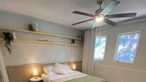 Une chambre à coucher avec un lit, des tables de chevet, un ventilateur de plafond et une fenêtre.