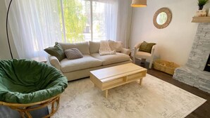 Un salon comprenant un canapé, un fauteuil vert, une table basse en bois, une suspension et une cheminée.