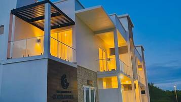 Un hôtel moderne à l’architecture contemporaine, avec deux étages, une entrée imposante et un espace extérieur aménagé avec des plantes en pot.