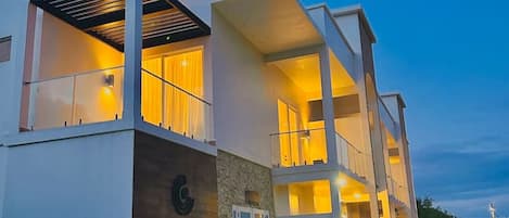 Ein modernes Hotel mit zweistöckiger Bauweise, einem markanten Eingangsbereich und einem begrünten Außenbereich mit Pflanzkübeln.