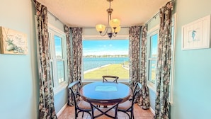 A dining area with a table and chairs, a chandelier, and a view of a beach and water. - Best Sunsets on the Lagoon Front w/ Pools & Pier (Gulf Shores)
