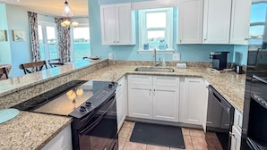A compact kitchen with white cabinets, a black stove, and a coffee maker. - Best Sunsets on the Lagoon Front w/ Pools & Pier (Gulf Shores)