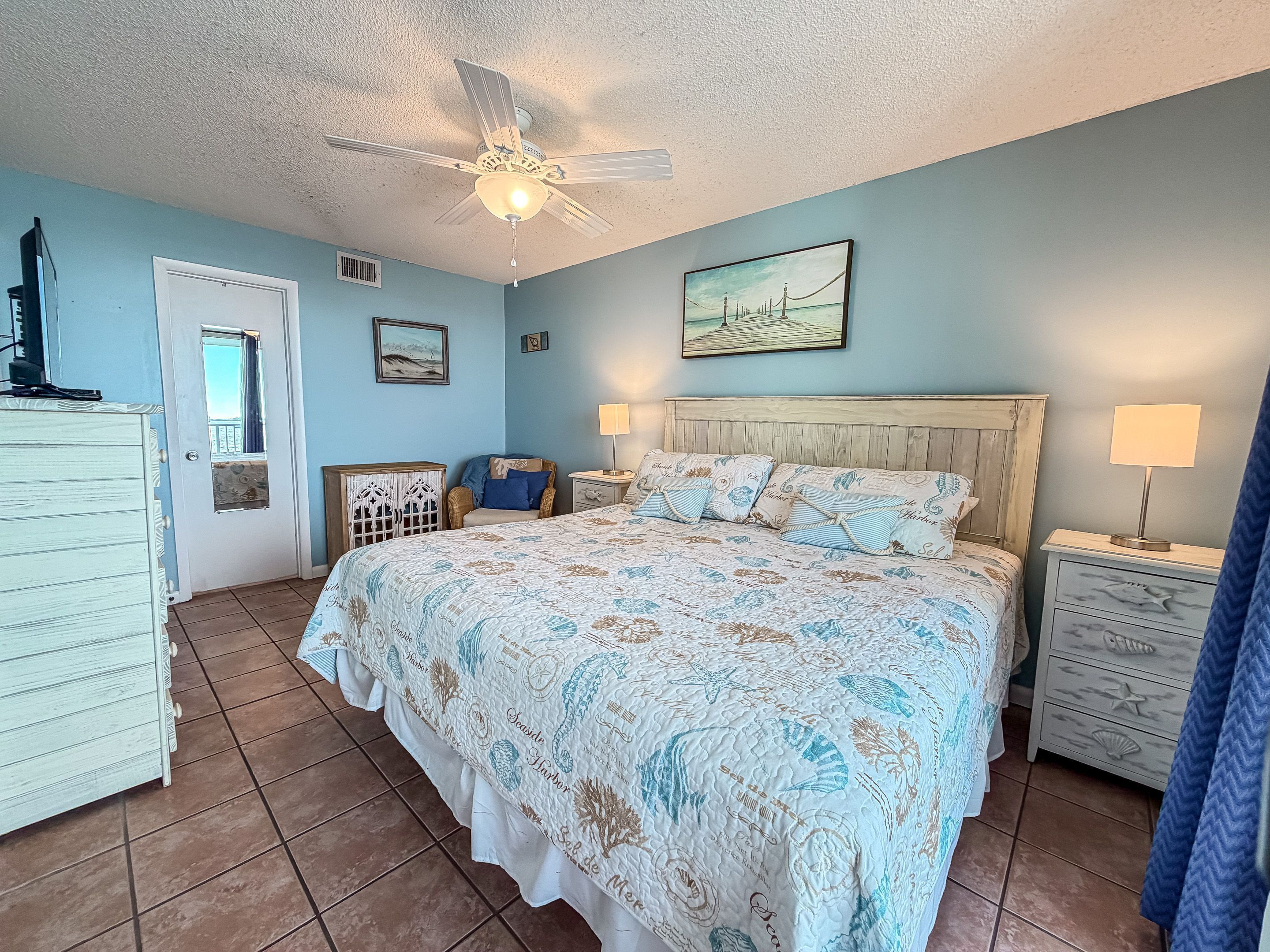 Une chambre à coucher avec un lit, deux tables de chevet, un ventilateur de plafond et une porte.