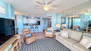 A living room with a sofa, armchairs, a TV, and a kitchen in the background. - Best Sunsets on the Lagoon Front w/ Pools & Pier (Gulf Shores)