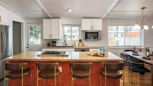 A modern kitchen with a central island, bar stools, and a dining area with a table and chairs. - The Wild Western: 5 BR, Hot Tub, Sauna, 2 Game Rooms, Putting Green, & more! (Denver)
