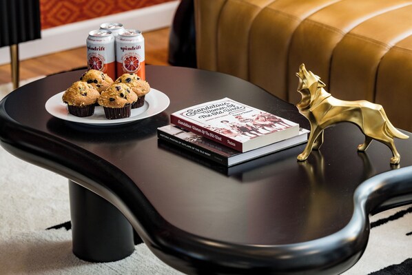 Een tafel met een boek, twee blikjes drinken en een bord muffins.