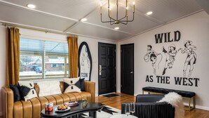 A modern living room with a leather sofa, a coffee table with snacks, a wall mural, and a chandelier. - The Wild Western: 5 BR, Hot Tub, Sauna, 2 Game Rooms, Putting Green, & more! (Denver)
