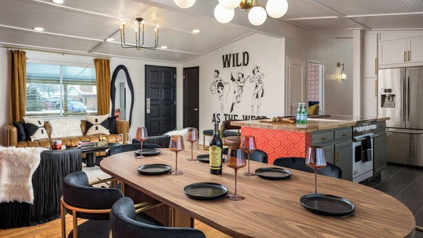 A modern dining area with a long wooden table, black chairs, and a chandelier. - The Wild Western: 5 BR, Hot Tub, Sauna, 2 Game Rooms, Putting Green, & more! (Denver)