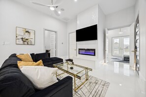 Een moderne woonkamer met een zwarte bank, een salontafel en een flatscreen televisie aan de wand.