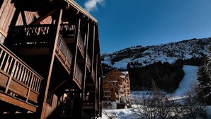 Ein Holzbalkongebäude vor einer Skipiste und einer verschneiten Landschaft.