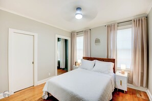 Un dormitorio con cama, mesitas de noche, un tocador, un espejo y una ventana con cortinas.
