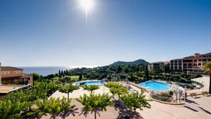 Ett semesterhotell med två pooler, utsikt över havet och ett kuperat landskap i bakgrunden.