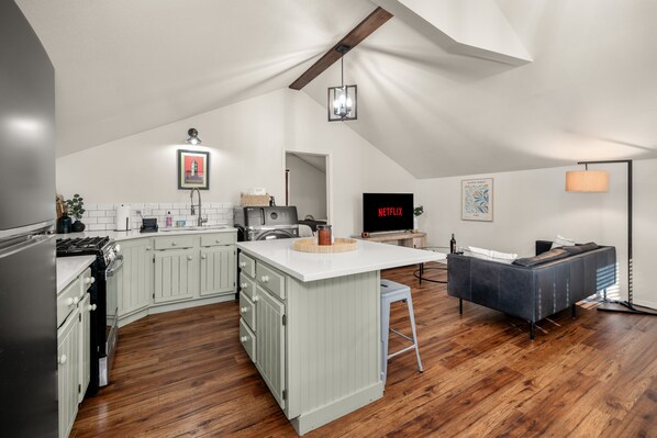 A modern kitchen with white cabinetry, a central island, and a dining area with a sofa. - The South Hill Nook, 4 min to Manito Park (Spokane)