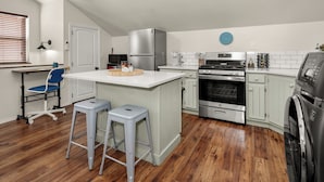 Una cocina con una isla central, horno empotrado, refrigerador de acero inoxidable y lavadora.