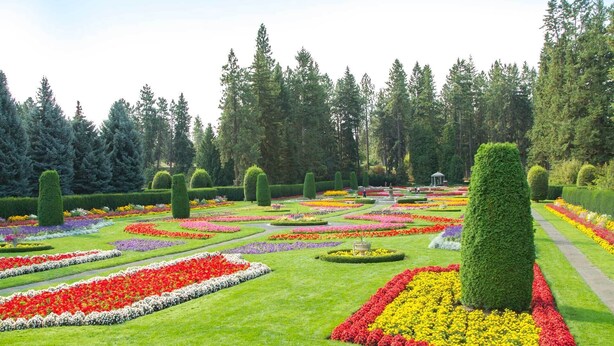 Un jardín formal con parterres de flores dispuestos geométricamente y setos cuidadosamente recortados.