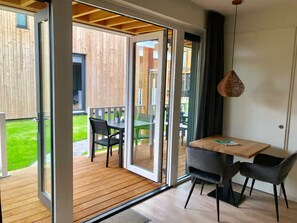 Une chambre moderne dotée d’une porte-fenêtre coulissante donnant sur un patio extérieur. La chambre est pourvue d’un plancher en bois, d’une petite table avec deux chaises et d’un luminaire suspendu.