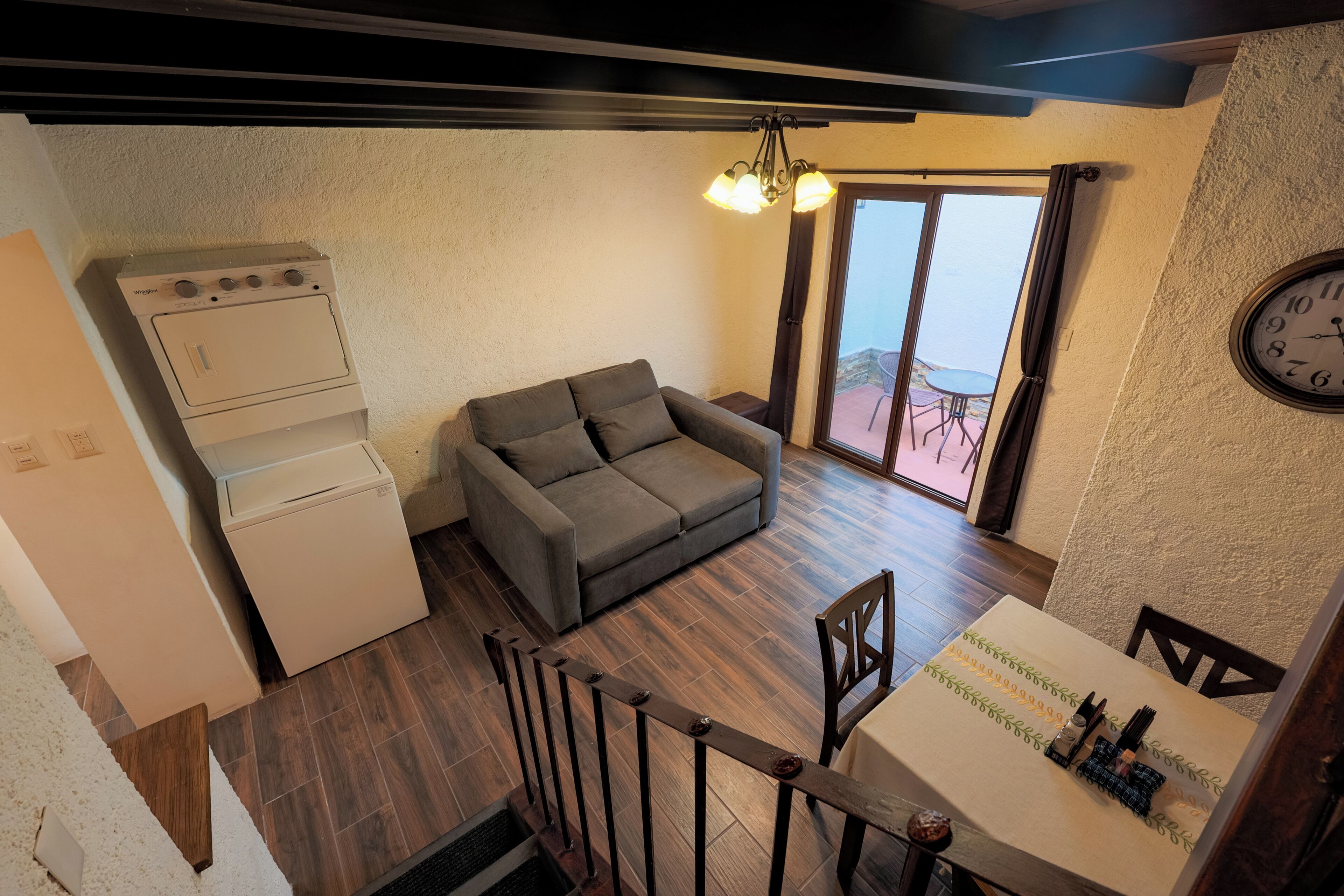 A compact living space with a kitchenette, a gray sofa, a dining table with chairs, and a view through a glass door.
