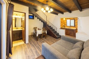 A living room with a sofa, a dining area with a table and chairs, a kitchen with a sink and cabinets, and a staircase.