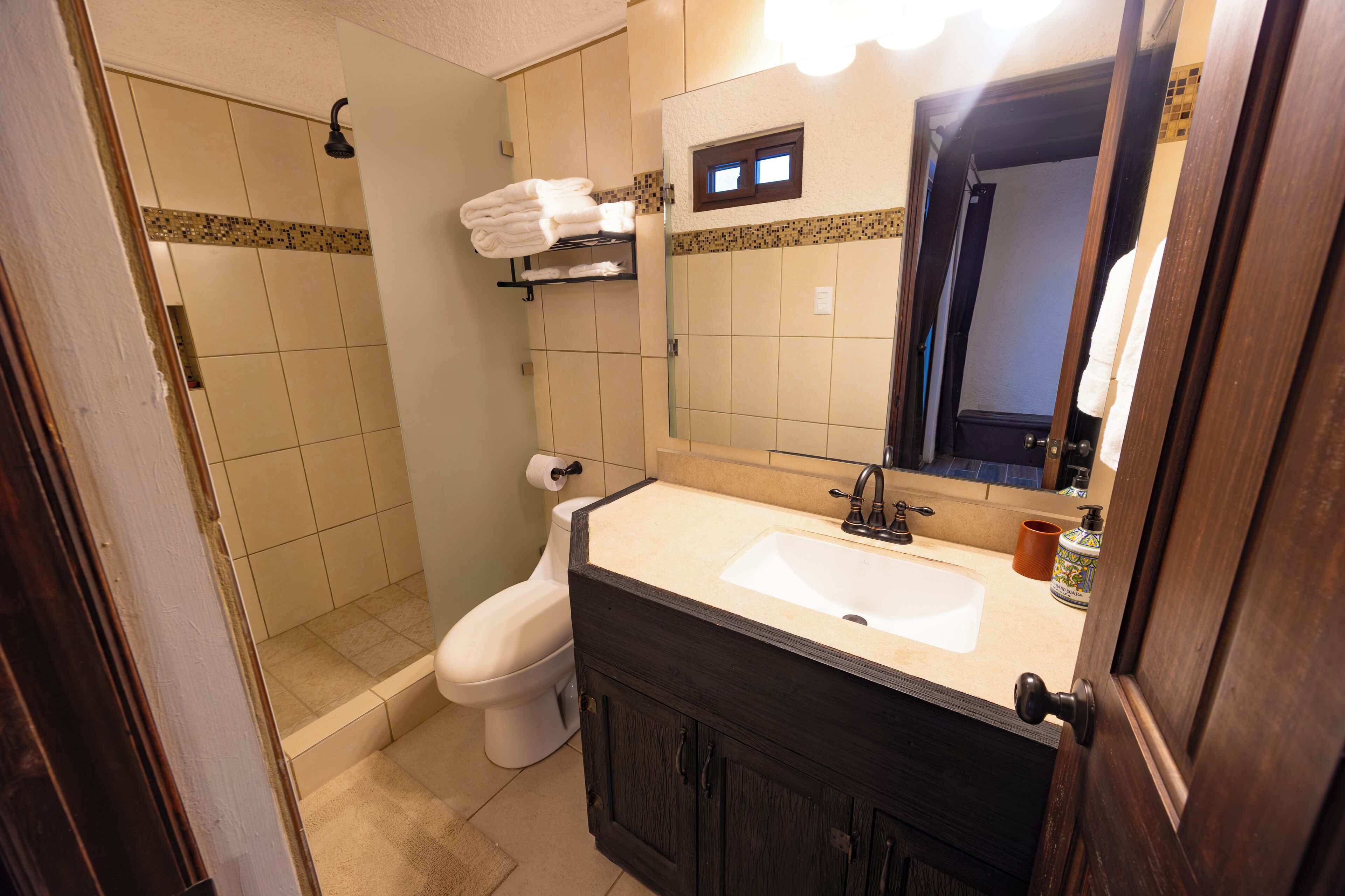 A bathroom with a shower, toilet, sink, and a mirror.