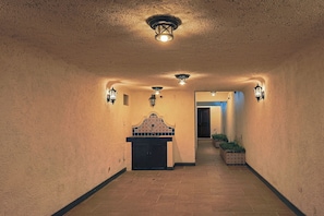 A hallway with textured walls, a decorative wall-mounted unit, and wall-mounted lighting fixtures.