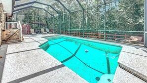 A covered outdoor swimming pool with a wooden deck and a red fence. - NEAR Fleming island LUXE-POOL-FIRE pit-games-more (Middleburg)