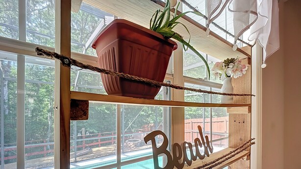 A window with a wooden shelf holding a potted plant and a sign that reads "Beach." - NEAR Fleming island LUXE-POOL-FIRE pit-games-more (Middleburg)