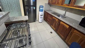 A kitchen with a gas stove, refrigerator, water dispenser, wooden cabinets, and a sink. - Exclusive Condominium Home - Resort Style Living with Pool and Parks 🌴🏊‍♂️ (Santa Cruz de la Sierra)