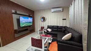 A modern living room with a flat-screen TV, a black leather sofa, a white armchair, and a glass coffee table. - Exclusive Condominium Home - Resort Style Living with Pool and Parks 🌴🏊‍♂️ (Santa Cruz de la Sierra)