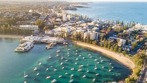 Vista aérea de una ciudad costera con un puerto deportivo, numerosos barcos y una combinación de edificios residenciales y comerciales.