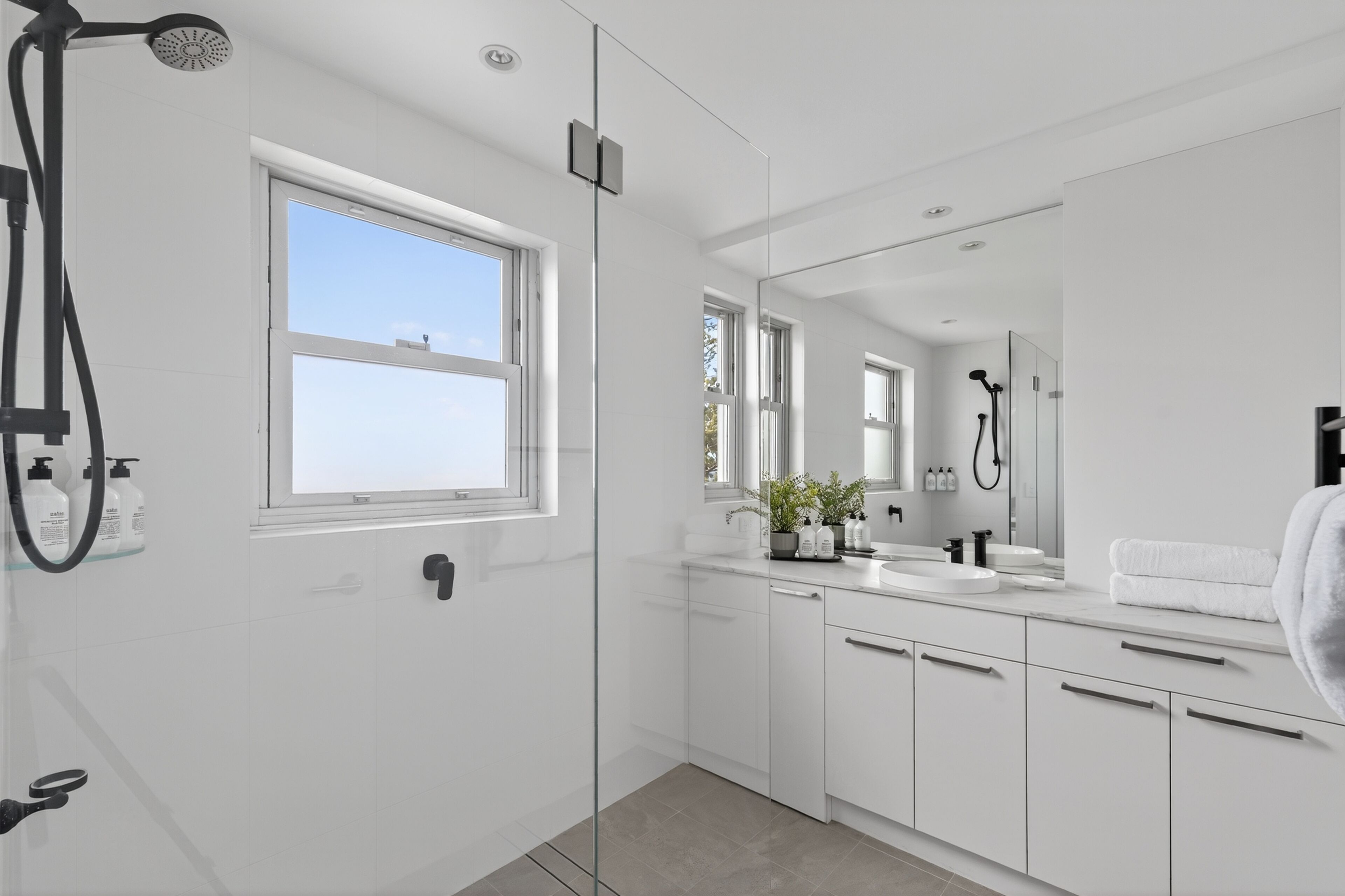 Une salle de bain moderne avec une douche à parois de verre, une grande fenêtre et un meuble-lavabo avec un miroir.