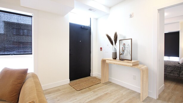 Una sala moderna con un sofá, una consola decorada con objetos, una puerta negra y vistas a un dormitorio.