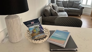 Una stanza con una lampada bianca, un cesto con una confezione di Kent Crisps e un libro degli ospiti su un tavolo.