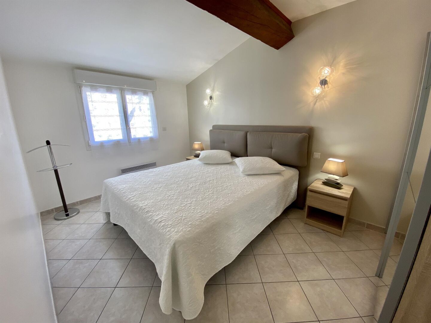 A bedroom with a large bed, two bedside lamps, a nightstand, and a window with curtains.