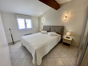 A bedroom with a large bed, two bedside lamps, a nightstand, and a window with curtains. - L'Ensoleillé - ROQUEFORT DES CORBIERES (ROQUEFORT DES CORBIERES)