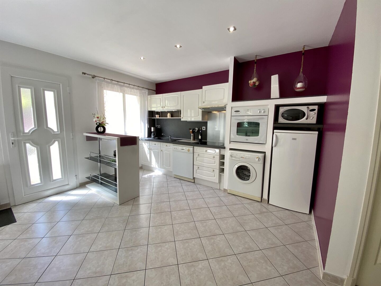 A modern kitchen with white cabinets, a built-in oven, microwave, and washing machine.