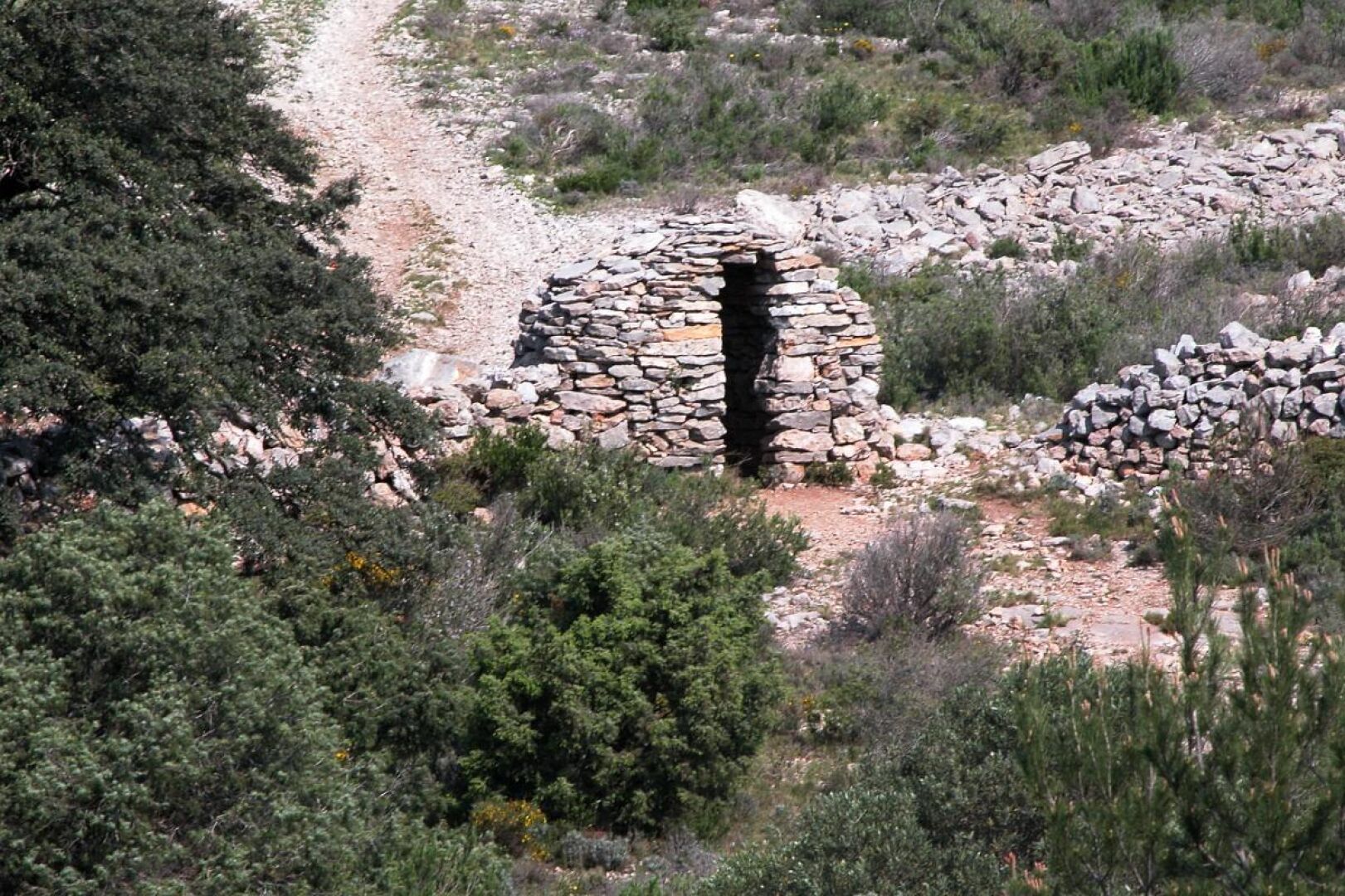 A stone structure with a central opening, surrounded by a natural landscape with sparse vegetation and a dirt path.