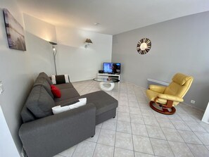 A modern living room with a grey sofa, a yellow armchair, a flat-screen TV, and a decorative wall clock. - L'Ensoleillé - ROQUEFORT DES CORBIERES (ROQUEFORT DES CORBIERES)