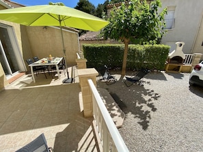 An outdoor patio with a table and chairs, a yellow umbrella, a tree, and a car parked nearby. - L'Ensoleillé - ROQUEFORT DES CORBIERES (ROQUEFORT DES CORBIERES)