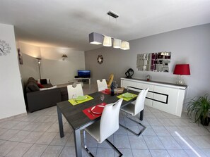 A modern living space with a dining area, a sofa, a television, and a kitchen area. - L'Ensoleillé - ROQUEFORT DES CORBIERES (ROQUEFORT DES CORBIERES)
