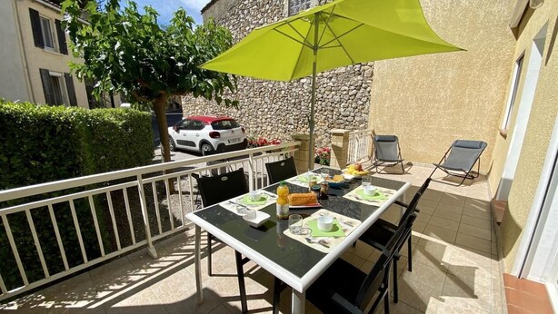 En udendørs terrasse med et bord dækket til morgenmad, en grøn parasol og en stengård i baggrunden.