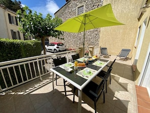 An outdoor patio with a table set for breakfast, a green umbrella, and a stone building in the background. - L'Ensoleillé - ROQUEFORT DES CORBIERES (ROQUEFORT DES CORBIERES)