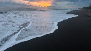 Une plage au sable sombre, bordée par des vagues.