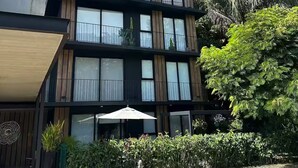 Un immeuble moderne à plusieurs étages, doté de balcons, d’un espace extérieur aménagé et couvert, et d’une végétation luxuriante.