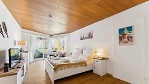 Une chambre spacieuse avec un plafond en bois, un grand lit, un bureau avec une lampe et une fenêtre avec des rideaux.