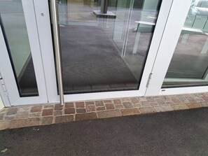 Une porte d’entrée en verre, avec un socle en pierre et un seuil en métal.