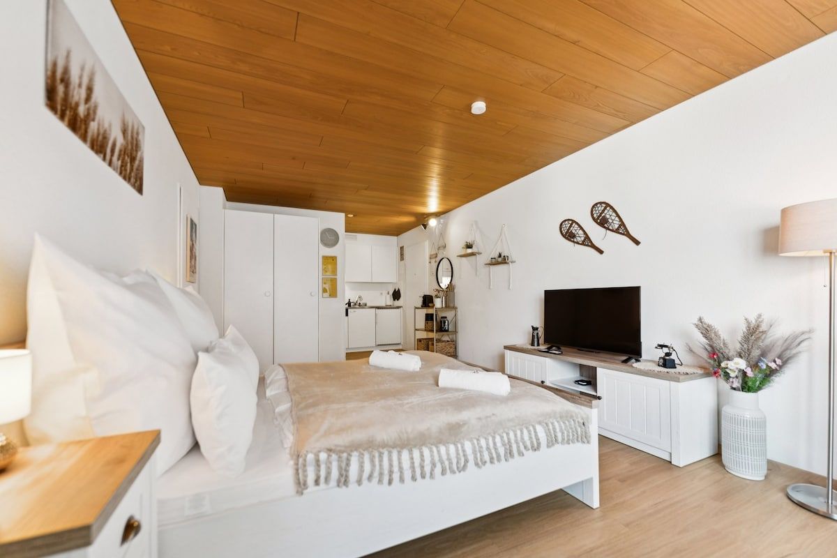 A modern bedroom with a wooden ceiling, a bed with white bedding, a TV, and a white cabinet.