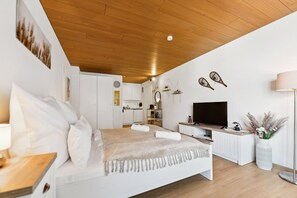 A modern bedroom with a wooden ceiling, a bed with white bedding, a TV, and a white cabinet.