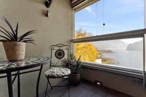 A balcony with a view of a body of water, a potted plant, a chair, and a table.