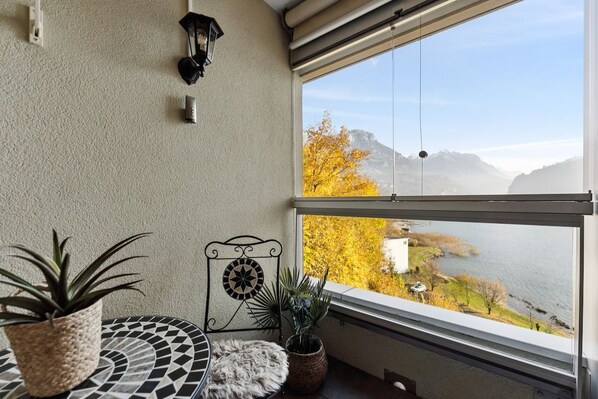 A balcony with a view of a lake and mountains, a potted plant, a decorative wall piece, and a textured rug.