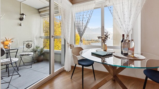 Un coin repas avec une table en verre, des chaises et une vue sur les montagnes, grâce à de grandes fenêtres.